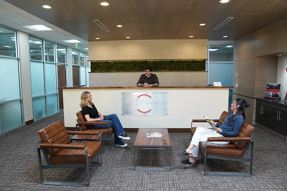 The reception lobby, with a preserved moss wall, a brushed REDPOINT CENTER sign on the desk front, a staff member behind the desk, and two people seated on benches.