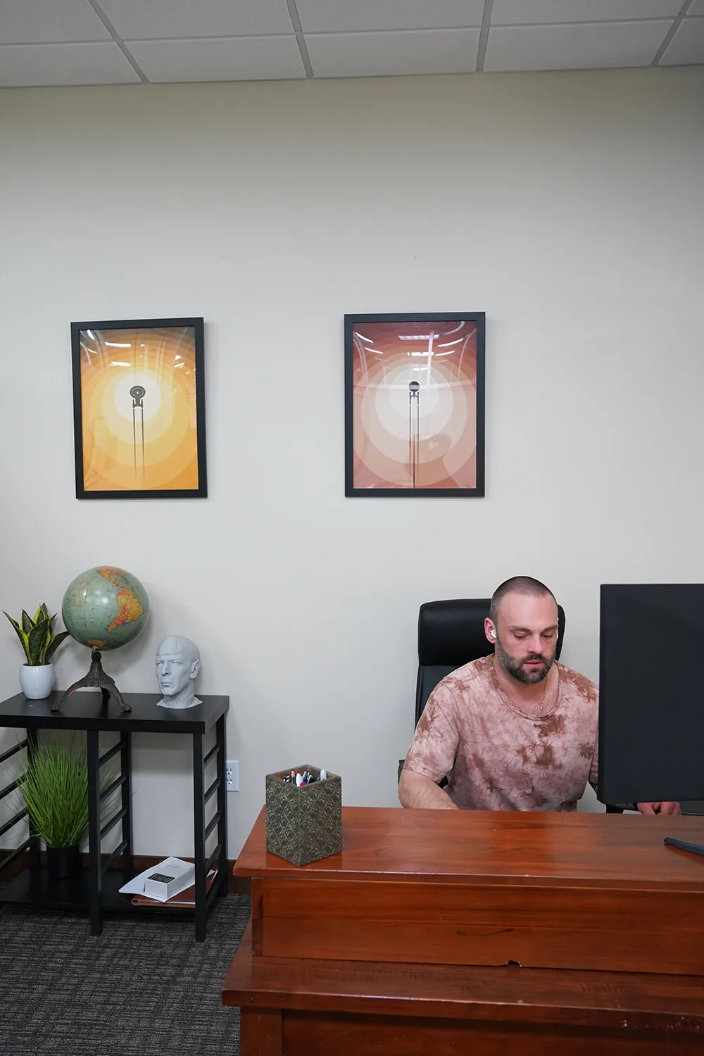 A staff member at a wood desk in a private office, with two framed dandelion prints and a globe on a side table.