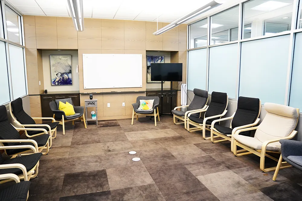 A ring of chairs facing a projector screen, framed by glass partitions.