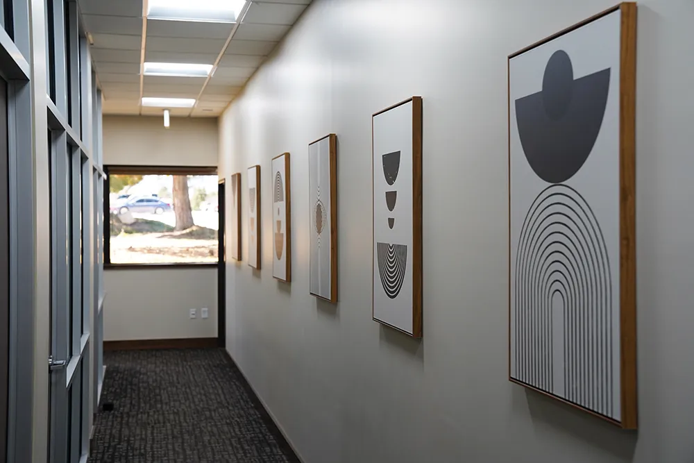 A corridor lined with framed abstract prints, with glass partitions along one side.
