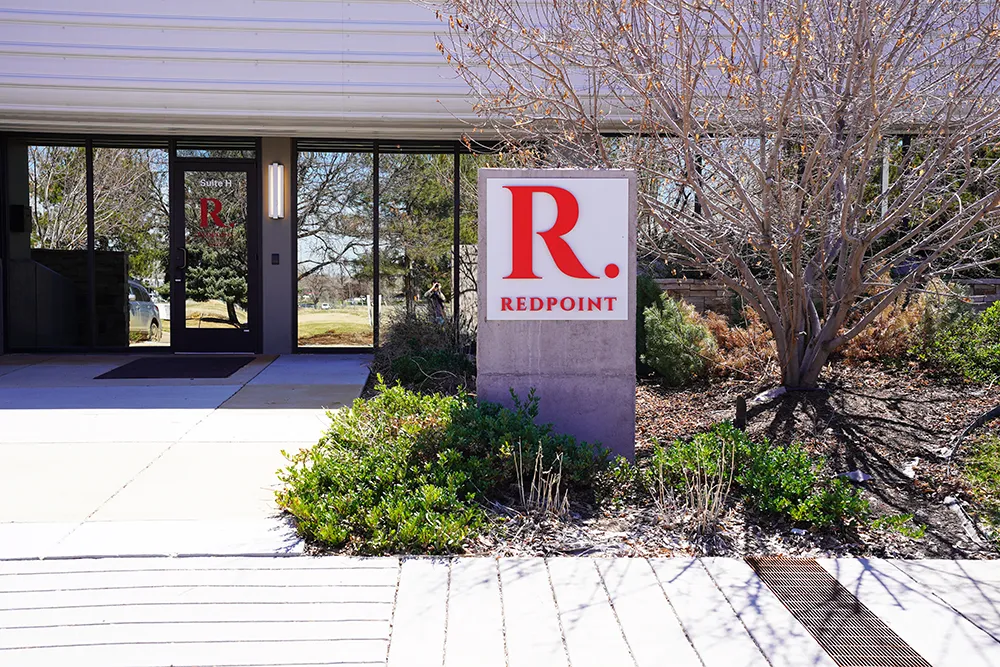 The glass entrance with the red R. REDPOINT banner, shrubs, and a sidewalk.