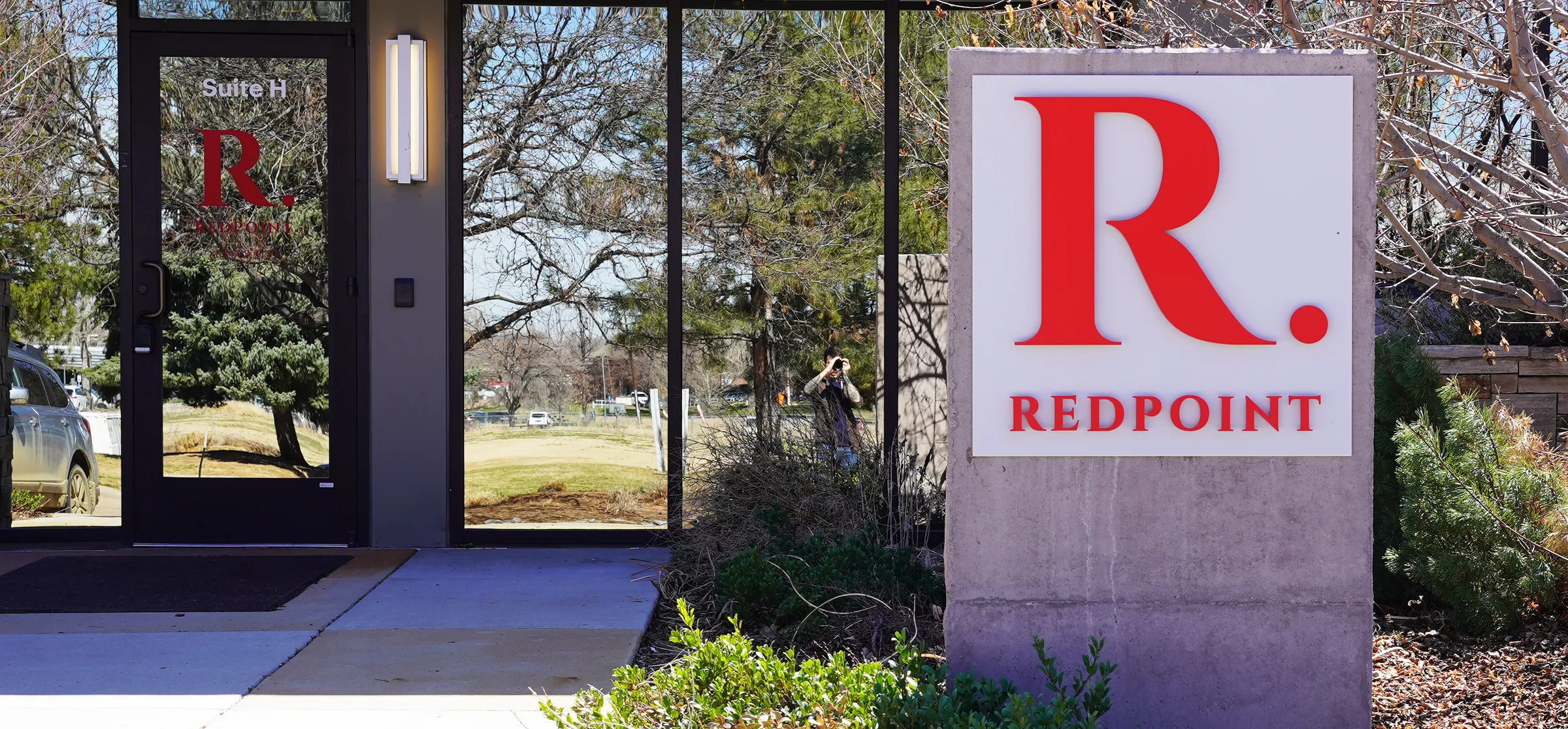 The entrance to a Redpoint Center office, with a glass door on the left and a concrete monument sign carrying the red Redpoint R logo on the right.