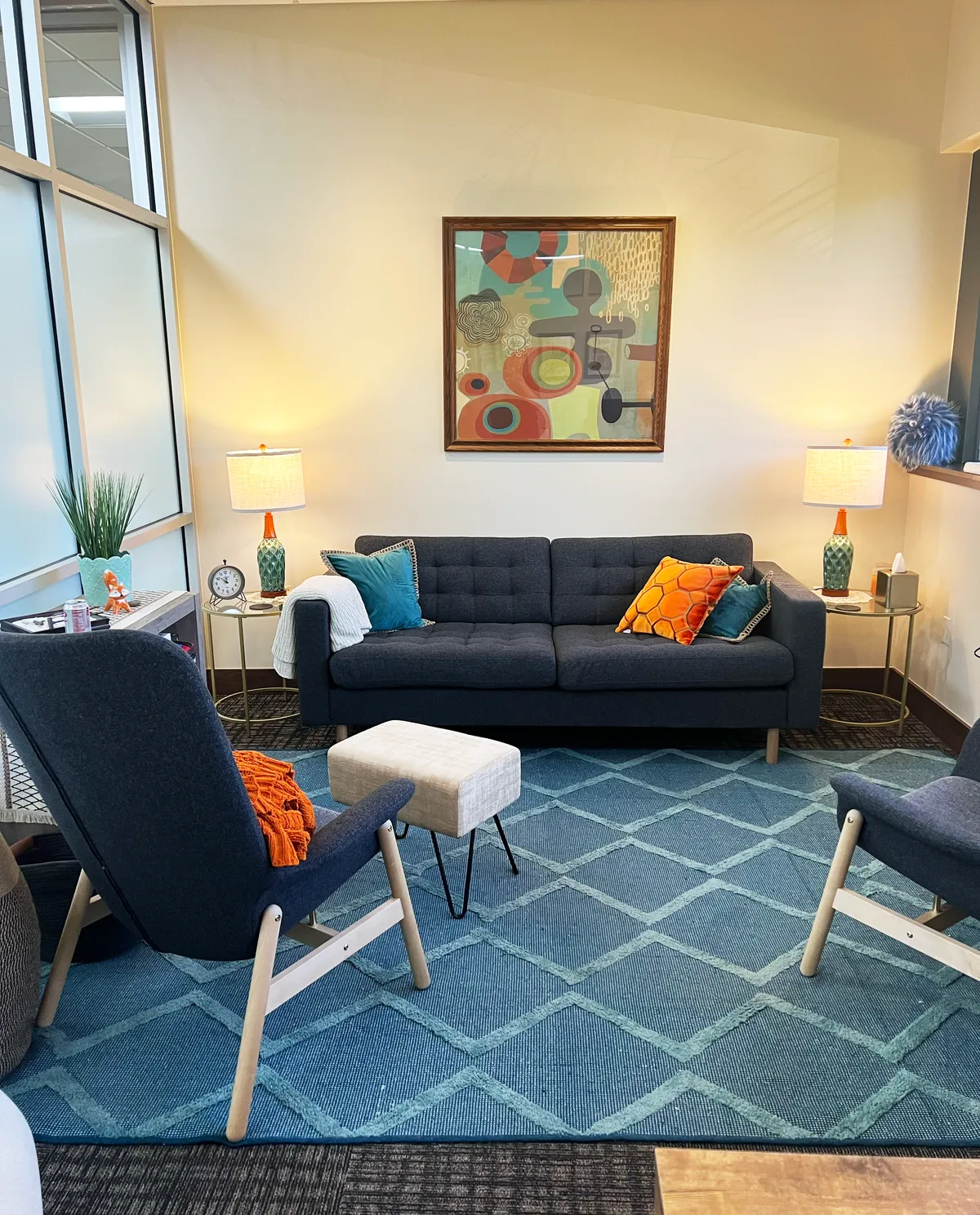 An empty Redpoint group lounge with a navy sofa, teal diamond rug, and two armchairs around a low ottoman.