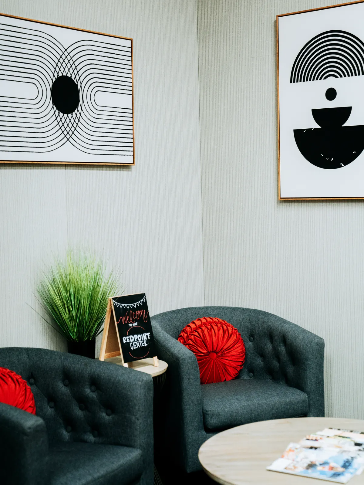 Two grey tufted armchairs with round red velvet cushions beside a small chalkboard sign reading 'Welcome to the Redpoint Center'.
