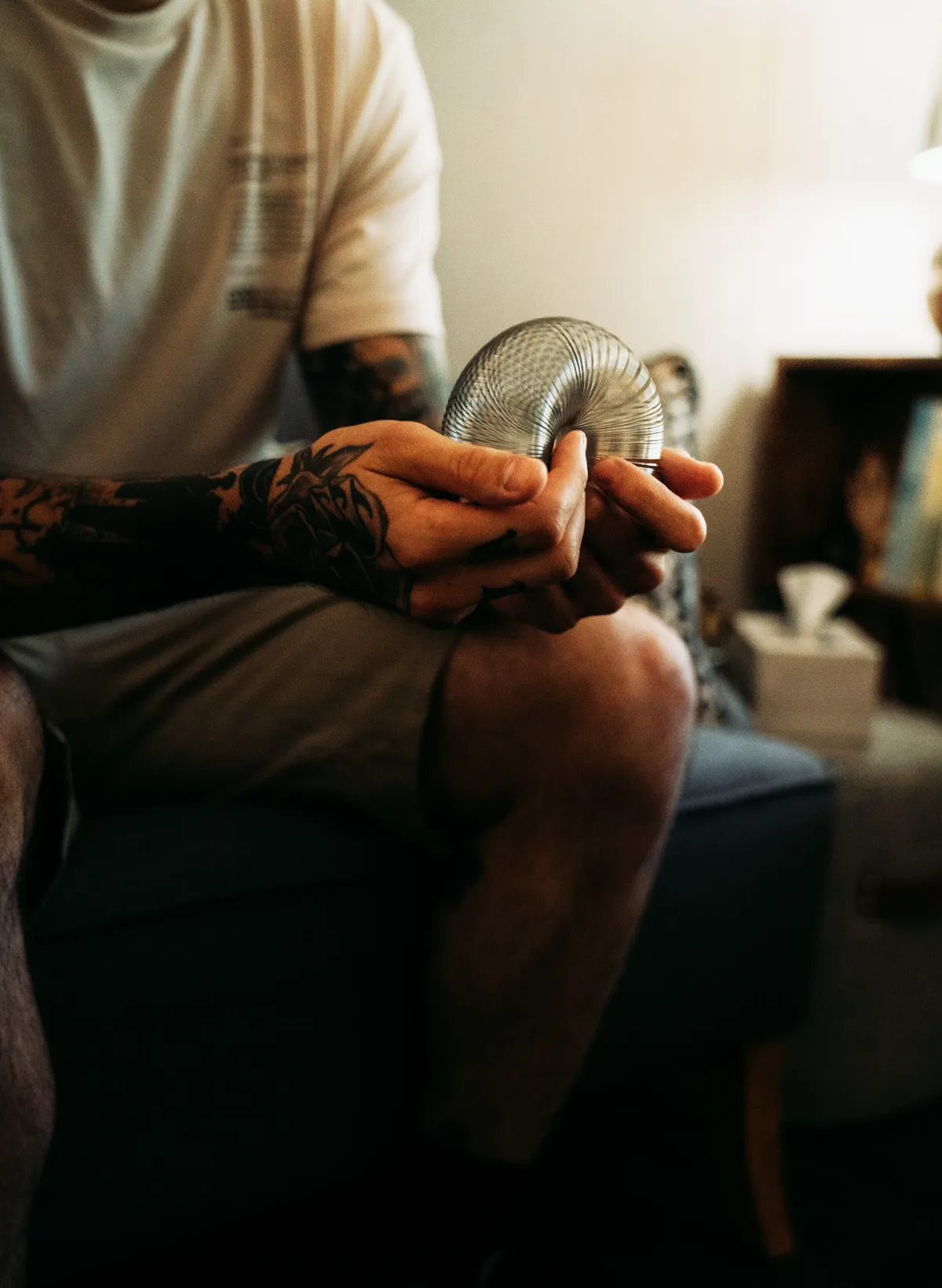 A man in a white tee holding a metal grounding coil, seated in a dim room.