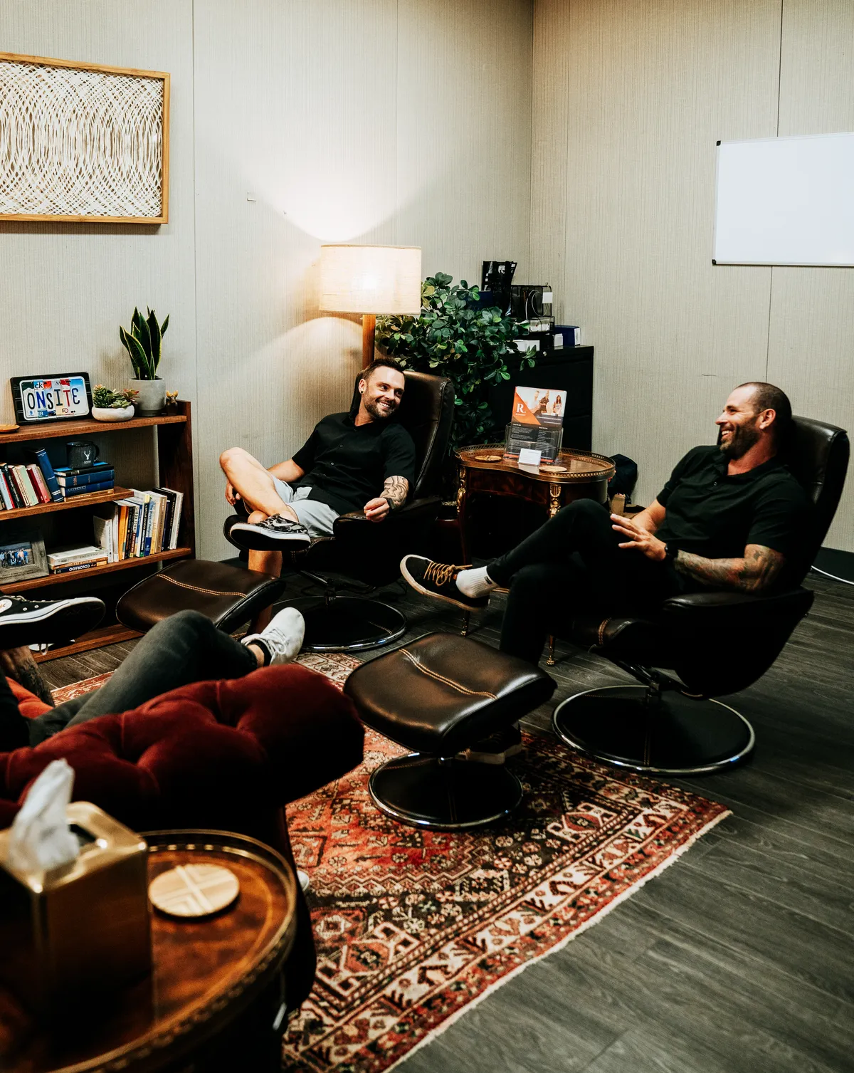 Two men in black shirts laughing in leather recliners in a book-lined Redpoint lounge.