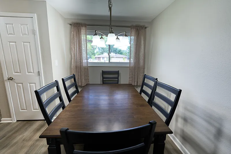 A long dark wood dining table with six chairs under a pendant light and a window at the back.